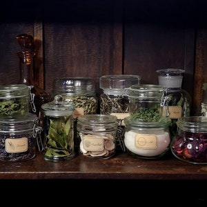 May include: A wooden shelf with a variety of glass jars filled with dried herbs and flowers. The jars have labels with handwritten text.