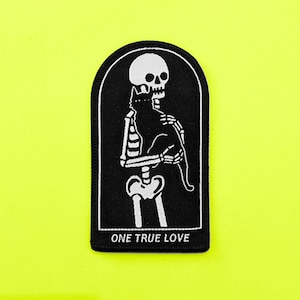Può includere: Toppa ricamata in bianco e nero con uno scheletro che tiene un gatto nero. La toppa ha uno sfondo nero e il testo "ONE TRUE LOVE" in basso.
