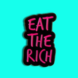 Puede incluir: Pin de esmalte negro con la frase "Eat the Rich" en letras rosas.