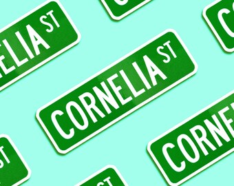 May include: Green street signs with white lettering that reads "Cornelia St." The signs are arranged in a repeating pattern on a light blue background.