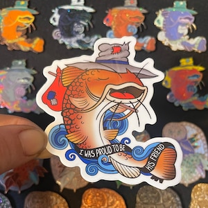 May include: A sticker featuring an orange catfish character with a gray hat and a red sack. The catfish is smiling and has the text "I WAS PROUD TO BE HIS FRIEND" on a blue wave design.