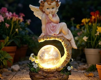 May include: A garden ornament featuring a cherub in a pink dress and flower crown, with a finger to its lips. The cherub sits on a curved branch above a glowing glass orb. The base is decorated with flowers, set in a garden setting.