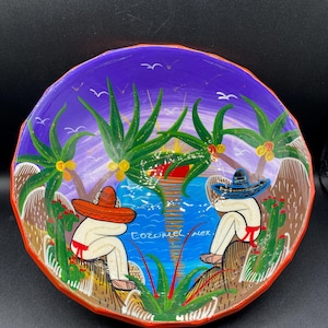 May include: Hand-painted ceramic bowl with a vibrant scene of two figures in sombreros, palm trees, and a sunset over the ocean. The bowl features the text "COZUMEL MEX" and is bordered with orange and red paint.