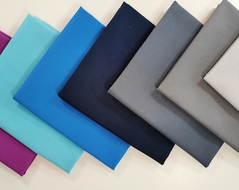 Op de afbeelding: Zes stofstalen in verschillende tinten blauw, teal, grijs en wit. De stalen zijn in een waaier vorm gerangschikt, met de donkerste tint bovenaan en de lichtste tint onderaan.