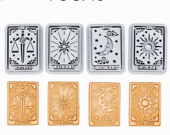May include: Two sets of six 3D printed cookie cutters in the shape of tarot cards. The top set is silver and the bottom set is gold. The cards are labeled with the names of the cards: Justice, The Star, The Moon, The Sun.
