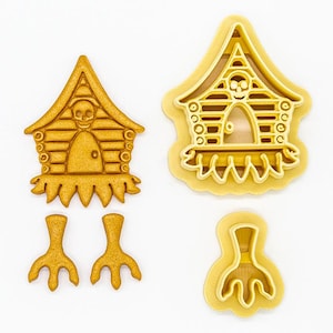 May include: A set of four cookie cutters in the shape of a witch's house and two witch's legs. The cutters are made of gold-colored metal.