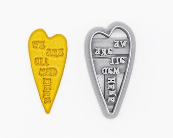 May include: A 3D printed heart-shaped cookie cutter made of plant-based plastic. The cutter is yellow and has the words "We are all made here" engraved on it. The cutter is shown next to a gray plastic mold of the same shape.