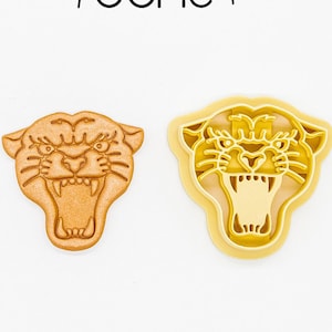 May include: Two 3D printed cookie cutters in the shape of a panther's head. The cutter on the left is brown and the cutter on the right is yellow. The text "3D PRINTED cutter" and "PLA plant-based plastic, non-toxic" is at the bottom of the image.