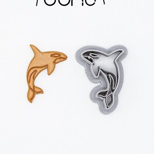 Op de afbeelding: Twee 3D-geprinte koekjesvormen in de vorm van orka's. De orka links is bruin en de orka rechts is grijs. De tekst "3D PRINTED cutter" en "PLA plant-based plastic, non-toxic" staat onderaan de afbeelding.