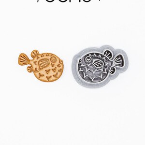 May include: A 3D printed cookie cutter in the shape of a pufferfish. The cutter is made of PLA plant-based plastic and is non-toxic. The cutter is shown in both its natural color and a gray color.