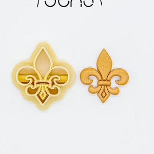 Peut inclure: Deux emportes-pièces en forme de fleur de lys imprimés en 3D. L'emporte-pièce de gauche est blanc et celui de droite est doré.