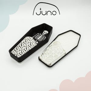 May include: Two black coffin-shaped containers with white designs. One container has a skeleton design and the other has a spiderweb design.