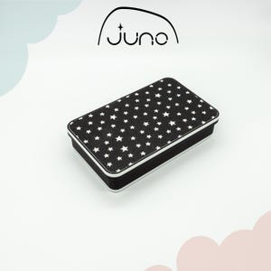 May include: Black rectangular tin box with a white star pattern. The lid has a white border. The box is sitting on a white surface. The text "Juno" is printed in black on a white background above the box.