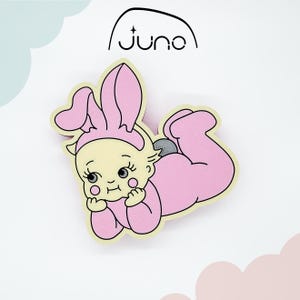 May include: A pink and yellow cartoon baby wearing bunny ears, lying on its stomach. The baby has a light yellow face and pink body, with the word "juno" in a black font above the baby.