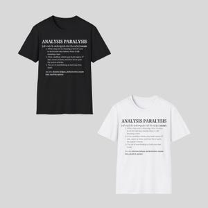 May include: Two t-shirts, one black and one white, each with the text "ANALYSIS PARALYSIS" and a definition. The definition includes the phrase "choosing a font" and other humorous descriptions of overthinking.