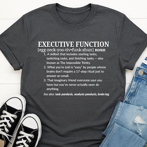 Puede incluir: Camiseta gris oscuro con la definición de "EXECUTIVE FUNCTION" impresa en blanco. La definición incluye una descripción humorística del término, junto con términos relacionados como "parálisis de tareas".