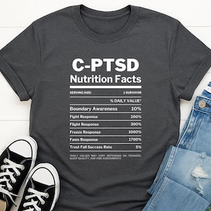 May include: A dark grey t-shirt displaying "C-PTSD Nutrition Facts" in white. The graphic resembles a nutrition label, detailing percentages for Boundary Awareness, Fight Response, Flight Response, Freeze Response, Fawn Response, and Trust Fall Success Rate.