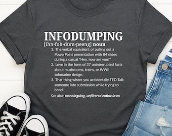 May include: Dark gray t-shirt with the word "INFODUMPING" in large white letters. The shirt includes a definition of the word, with examples. The shirt is paired with jeans and sneakers.