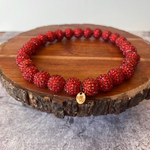 May include: A red beaded necklace with a gold tag. The beads are covered in small red rhinestones.