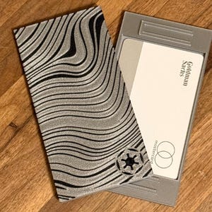 May include: A set of three ceramic mugs with a speckled, matte finish. The mugs are in shades of cream, light gray, and dark gray. Each mug has a simple, minimalist design and a rounded handle.