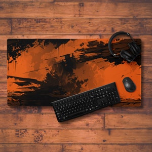May include: A black and orange gaming desk mat with a splatter paint design. A black keyboard and mouse are on the mat. A pair of black headphones are on the wooden surface behind the mat.