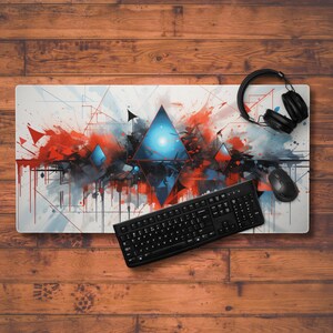 May include: A white desk mat with a geometric abstract design featuring red, blue, and black paint splatters. A black keyboard and a black mouse are on the mat.