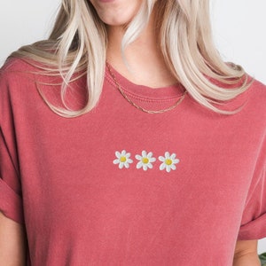 Peut inclure: Un t-shirt rouge avec trois marguerites brod&eacute;es blanches.