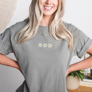 Peut inclure: Un t-shirt gris avec trois marguerites blanches brod&eacute;es.