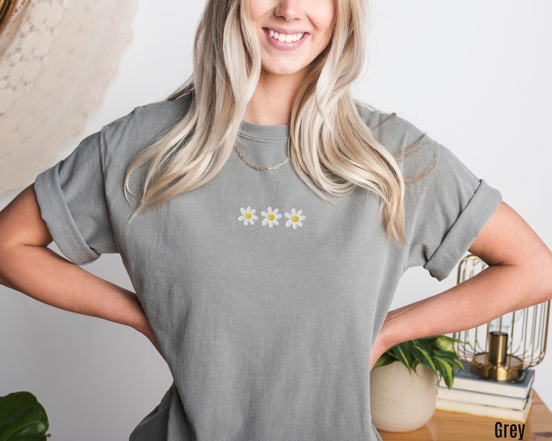 Peut inclure: Un t-shirt gris avec trois marguerites blanches brod&eacute;es.