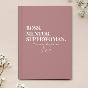May include: A pink notebook with the text "BOSS. MENTOR. SUPERWOMAN. Thanks for being the best Jessica" in white lettering.