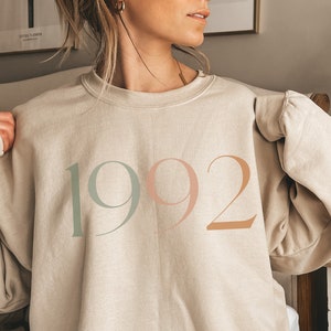 May include: A beige sweatshirt with the year "1992" printed on the front in green, pink, and orange.