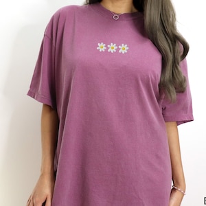 Peut inclure: Un t-shirt surdimensionn&eacute; mauve avec une rang&eacute;e de trois marguerites blanches brod&eacute;es avec des centres jaunes.