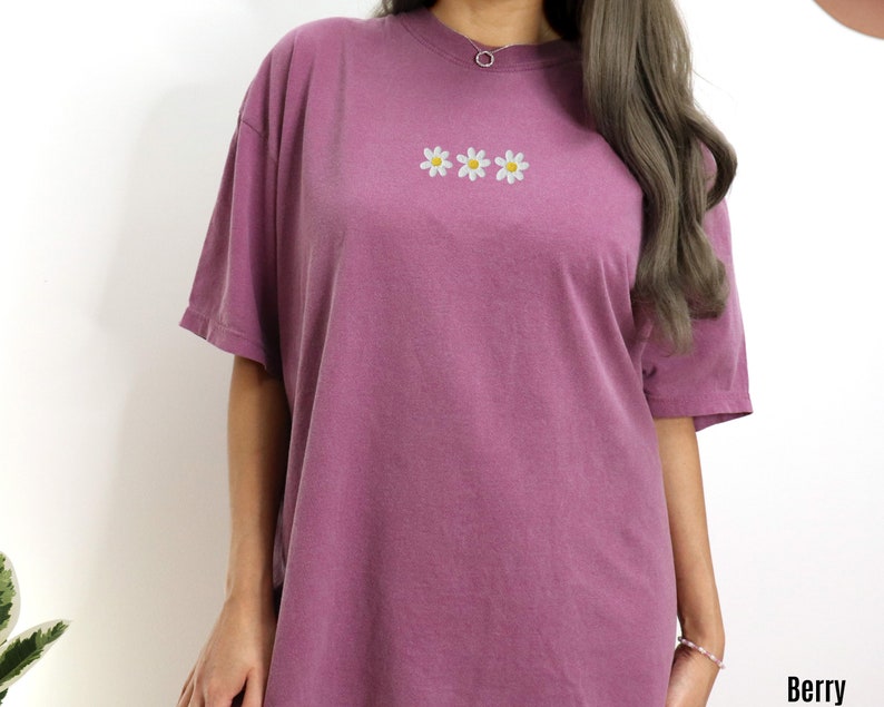 Peut inclure: Un t-shirt surdimensionn&eacute; mauve avec une rang&eacute;e de trois marguerites blanches brod&eacute;es avec des centres jaunes.