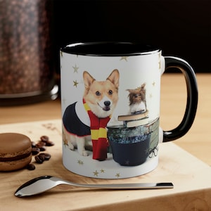 May include: A white ceramic mug with a black rim and handle. The mug features a colorful illustration of a corgi wearing a wizard's robe and scarf, standing next to a small owl perched on a stack of books. The background is white with gold stars.
