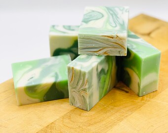 May include: Four bars of handmade soap with a green and white marbled design. The soap is stacked on a wooden cutting board.