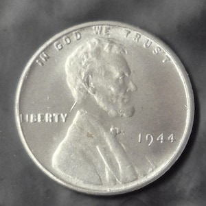 May include: A close-up of a silver 1944 Lincoln penny. The coin features the profile of Abraham Lincoln, the word "LIBERTY", and the phrase "IN GOD WE TRUST". The year "1944" is also visible.