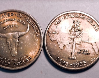 May include: Two silver half dollar coins. One coin features a longhorn and the text "United States of America" and "Half Dollar". The other coin has a map and the text "Old Spanish Trail 1535-1935".