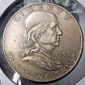 May include: A silver coin featuring a profile of Benjamin Franklin, with the inscription "LIBERTY" at the top and "IN GOD WE TRUST" at the bottom. The year "1953" is visible. The coin is encased in a protective holder.