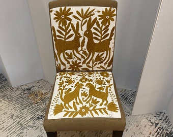 May include: A brown chair with a white fabric seat and back. The fabric features a gold embroidered design of rabbits and flowers.