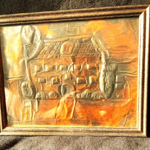 May include: A rectangular wall art piece featuring a metallic embossed house scene with a dark brown wooden frame. The artwork displays a house with a tiled roof and windows, rendered in shades of copper, bronze, and dark metallic tones.