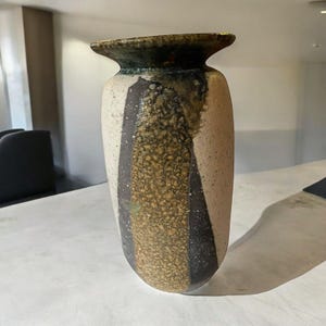 May include: A ceramic vase with a white, brown, and gold glaze. The vase has a wide mouth and a narrow base.