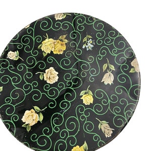 May include: A black and green round plate with a floral pattern. The plate is decorated with yellow roses and green swirls.