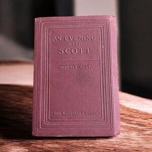 May include: A small, vintage book titled "An Evening with Scott" by Sherwin Cody. The book has a textured, mauve cover with embossed lettering and decorative borders. The book is part of "The Nutshell Library".