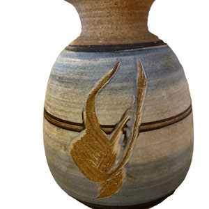 May include: Handmade ceramic vase with a bulbous body and a narrow neck. The vase features a blue and tan color scheme with a brown accent band and a textured, abstract design in shades of brown and tan.
