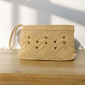 May include: A beige crocheted clutch bag with a brown wooden bead design. The bag has a single strap.