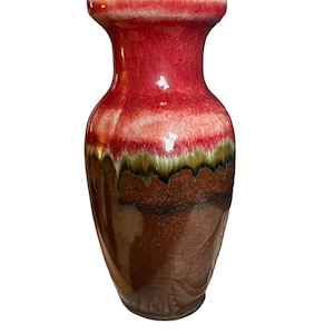 Puede incluir: Un jarrón de cerámica rojo y marrón con un borde blanco. El jarrón tiene un esmalte moteado con tonos de rojo, marrón y verde.