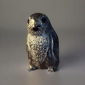 Puede incluir: Una pequeña figura de pingüino hecha a mano. El pingüino es principalmente de color gris oscuro con detalles moteados blancos en el pecho. Tiene ojos negros y un pico pequeño y abierto. La escultura está de pie y parece estar hecha de piedra o un material similar.