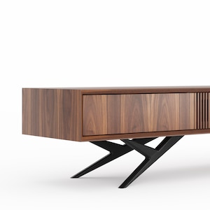 May include: A contemporary wooden cabinet in a dark walnut finish. It has a single drawer and a vertical slatted design. The cabinet is supported by black, angular metal legs, giving a floating effect. The cabinet's dimensions are approximately 150cm in length.