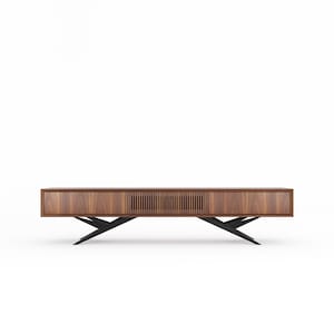May include: A contemporary media unit in warm-toned wood, featuring a linear grain. It has two drawers and a slatted centre section. The unit is supported by a black, angular metal base, giving a floating effect. The design is minimalist and modern, suitable for a living room.