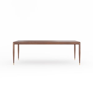Op de afbeelding: Een lange, rechthoekige houten tafel met een donkerbruine afwerking. De tafel heeft vier slanke, taps toelopende poten met messingkleurige accenten aan de basis. Het ontwerp is minimalistisch en modern, geschikt om te dineren of als bureau, ongeveer 200 cm lang.
